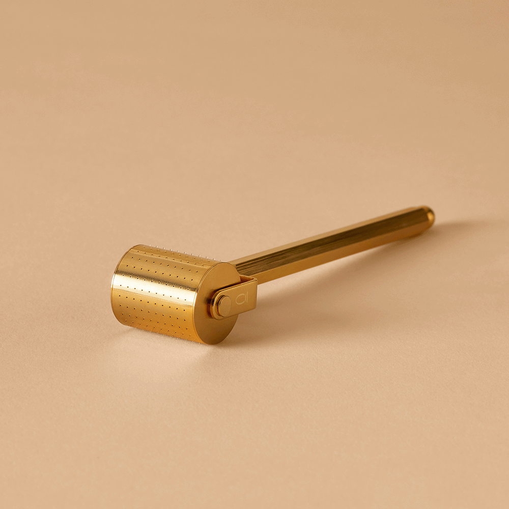 Gold Divine Ritual™ Derma Roller on a nude coloured background