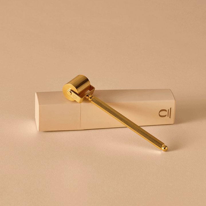 Gold Divine Ritual™ Derma Roller propped up on a nude crystal case