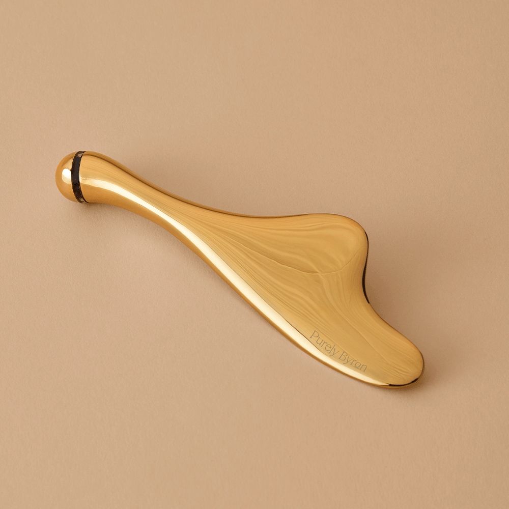 Woman holding a gold Divine Ritual™ Face Sculptor on a nude coloured background