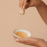 Woman using dropper from a mask booster to add the concentrate to the clay mask in a ceramic bowl